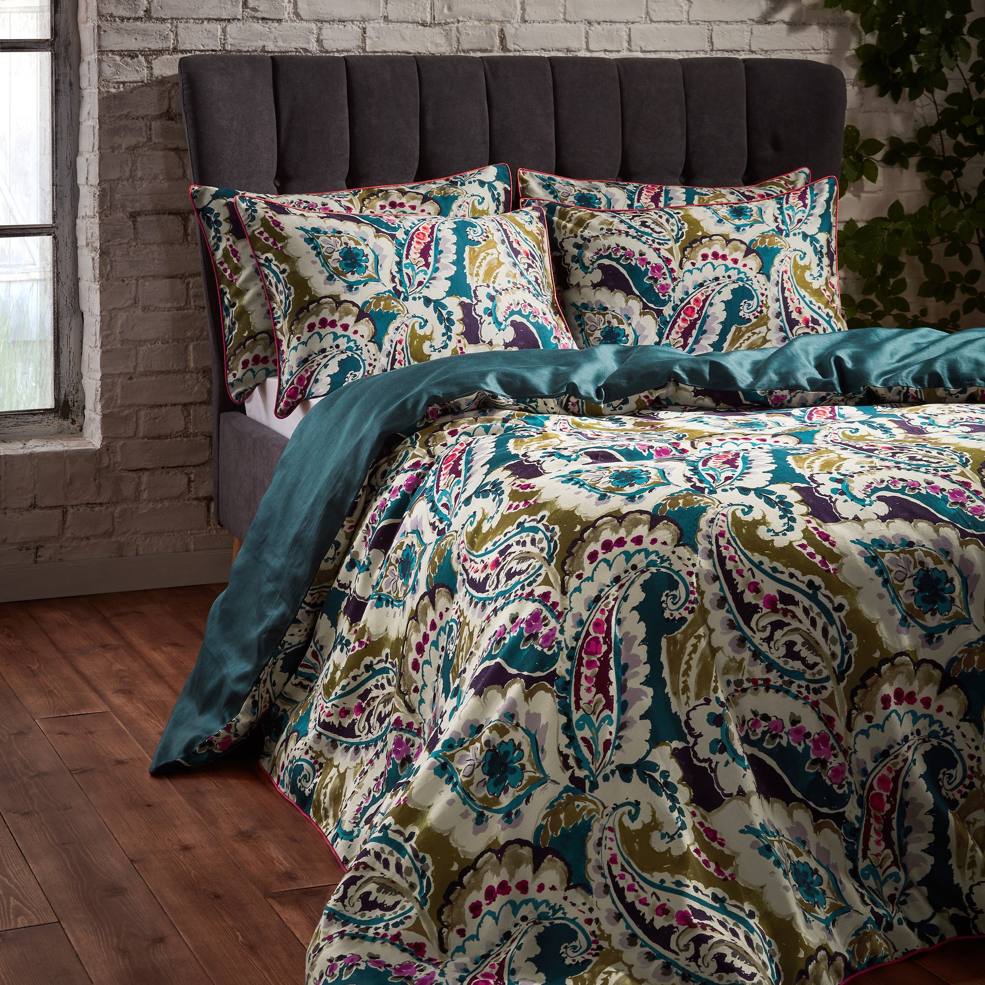 Side view of the luxury Aretha Paisley Pattern Duvet Cover Bed set with a dark green headboard and rustic tiled back wall, duvet folded over to show reversible green underside with a silky sheen