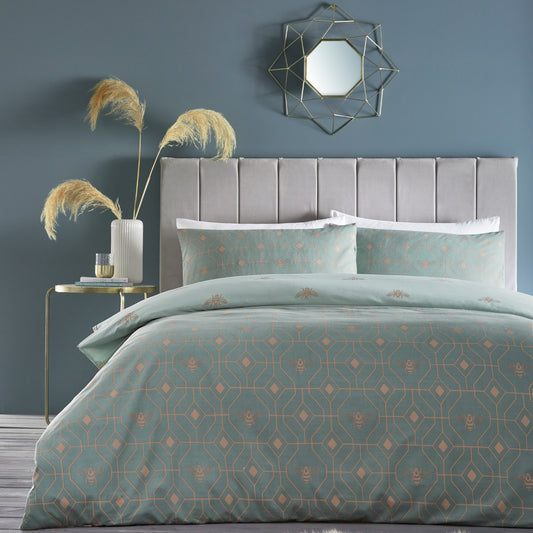 Beautiful luxury duvet cover bedding set with a geometric pattern and small bees in each geometric shape, grey headboard and sliver accent mirror above on the wall. Bedding is in eau de nil sage colour. 