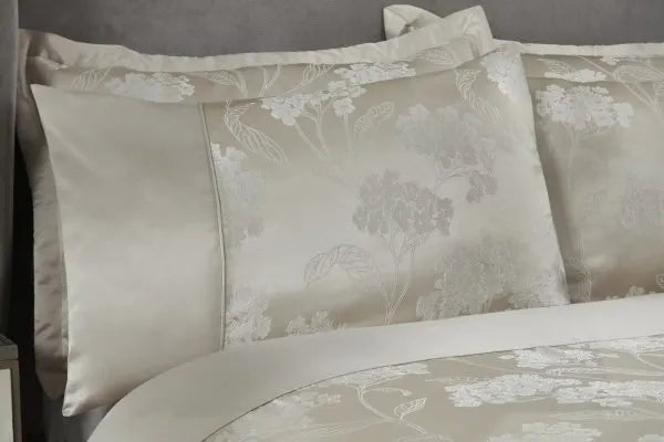 Close up of double bed with grey headboard from a side view  showing half the bed. Displaying the English Garden Collection Embellished Jacquard Duvet Double Bedding Cover Set in Cream. A third of the pillow is plain satin sheen and the rest of the pillow shows the delicate, floral pattern.