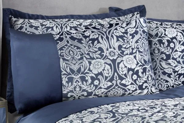 Close up of double bed with grey headboard showing two pillows from a side view displaying the Harrow Collection Embellished Jacquard Duvet Double Bedding Cover Set in Navy Blue with silver embroidery and sateen finish. 