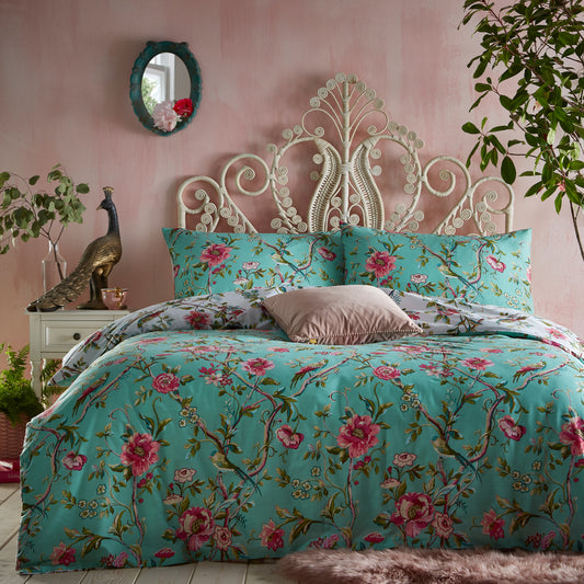 Beautiful, luxury bedding set with pink flowers and green leaves in a vintage style and jade background with little birds. Accent jade mirror on the wall, french style headboard and peacock statement ornament on side table.