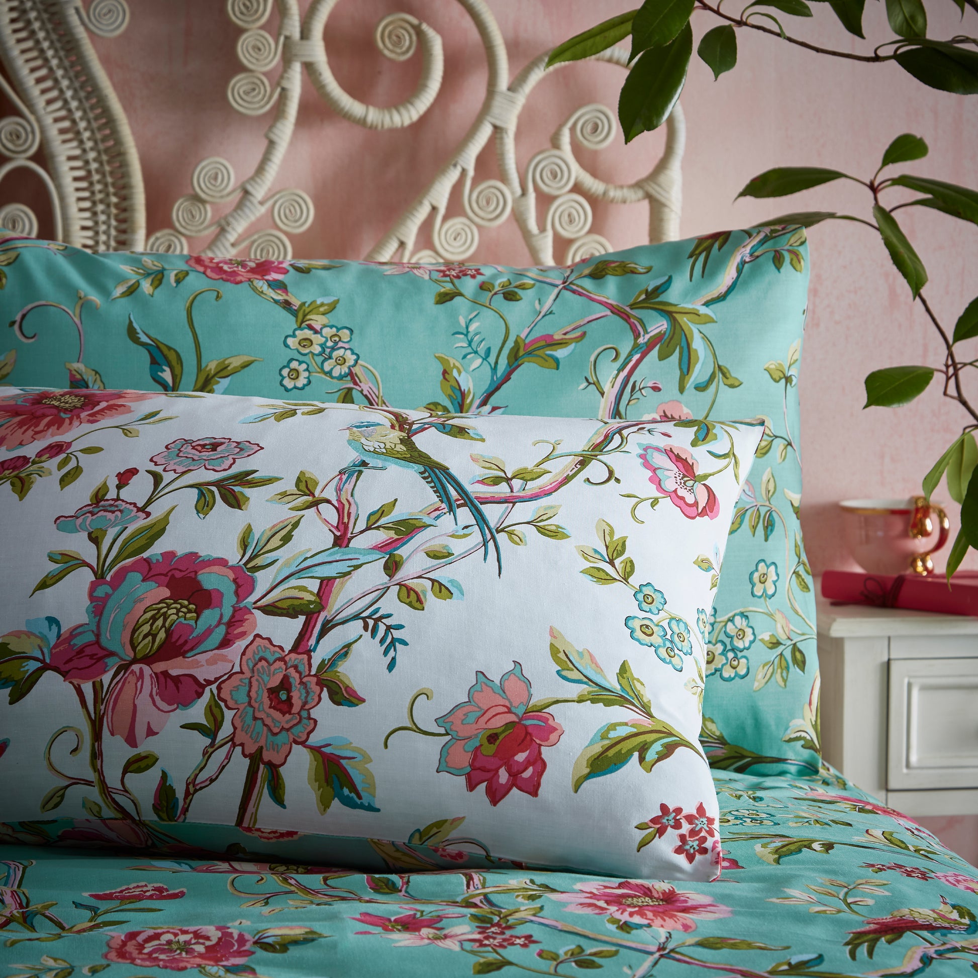 Close up of two beautiful pillows with pillowcase in a luxury bedding set with pink flowers and green leaves in a vintage style and jade background