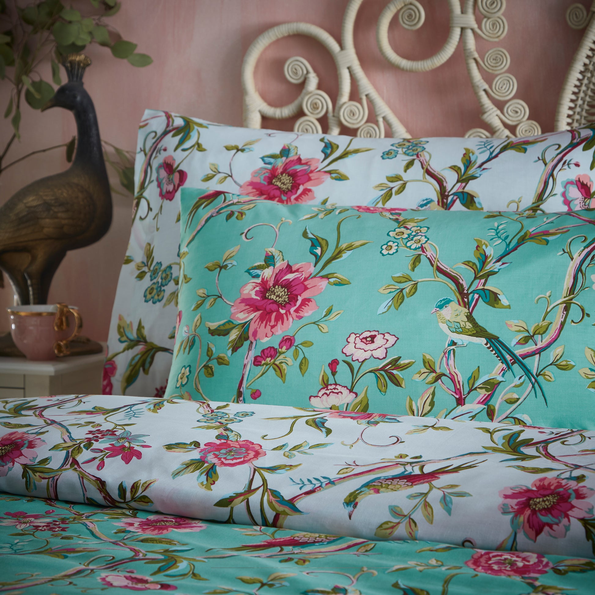 Close up of two beautiful pillows with pillowcase in a luxury bedding set with pink flowers and green leaves in a vintage style and jade background against a headboard